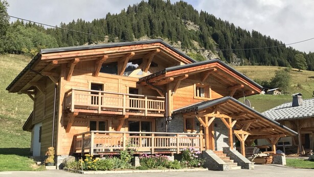 Eine Holzhütte mit Balkon, Steinstufen und einem Berg im Hintergrund.