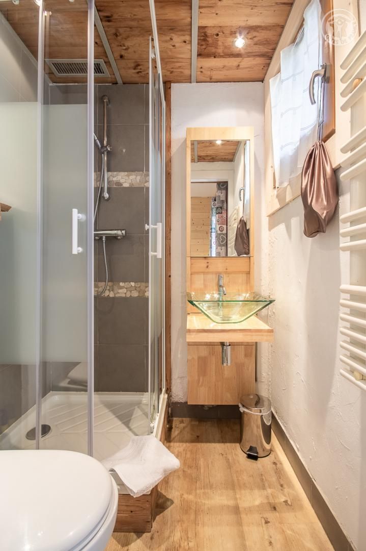 Ein Badezimmer mit Duschkabine aus Glas, einem Holzbadezimmermöbel mit Waschbecken aus Glas und einer weißen Toilette.