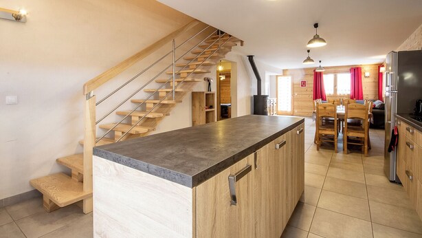 A modern kitchen with a central island, wooden staircase, and a dining area with a table and chairs. - LE Chenavelle D'en Haut (HAUTELUCE LES SAISIES)