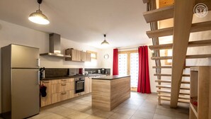 A modern kitchen with a central island, stainless steel appliances, wooden cabinets, and a red curtain. - LE Chenavelle D'en Haut (HAUTELUCE LES SAISIES)