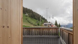 A wooden balcony with a view of a hilly landscape, a ski lift, and a building in the distance. - LE Chenavelle D'en Haut (HAUTELUCE LES SAISIES)