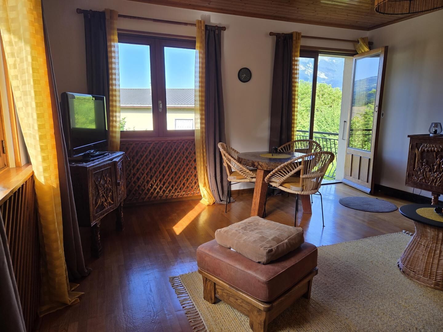 A room with a television, a dining table with chairs, a sofa, and a view of the outdoors.