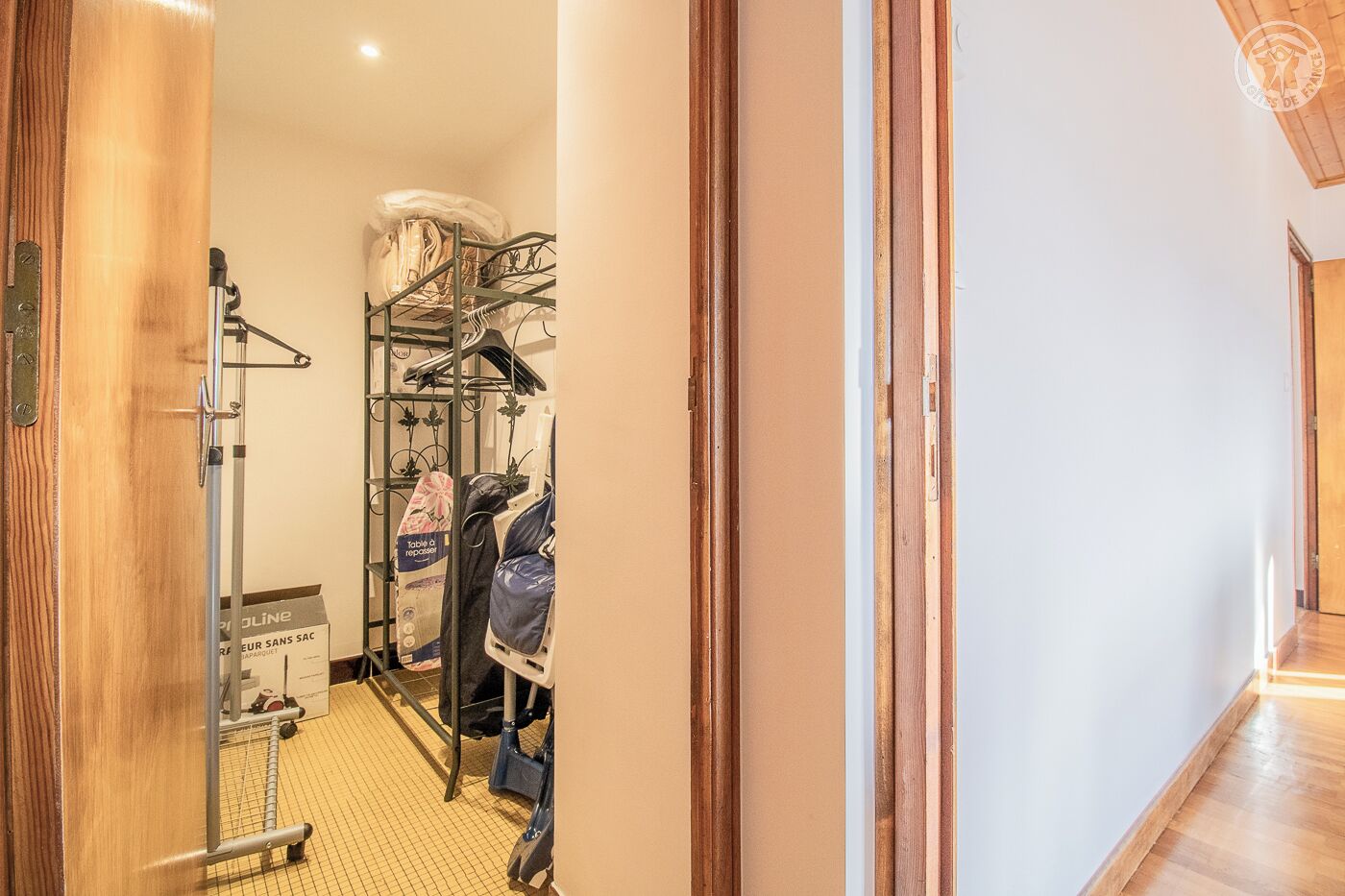 A hallway leading to a room with a wooden door, a metal rack with clothes, and a box labeled "POLINE".