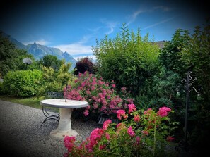 Ein Garten mit einem runden Tisch und Stühlen, umgeben von üppigem Grün und rosa Blüten.