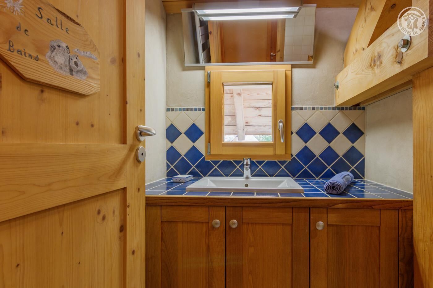 Un baño de madera con lavamanos, espejo y un salpicadero de azulejos azules.