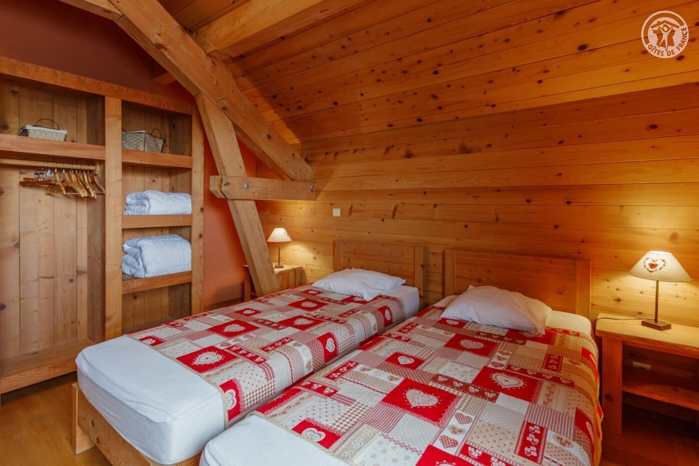A cozy wooden cabin room with two beds, a wooden wardrobe, and two bedside lamps.