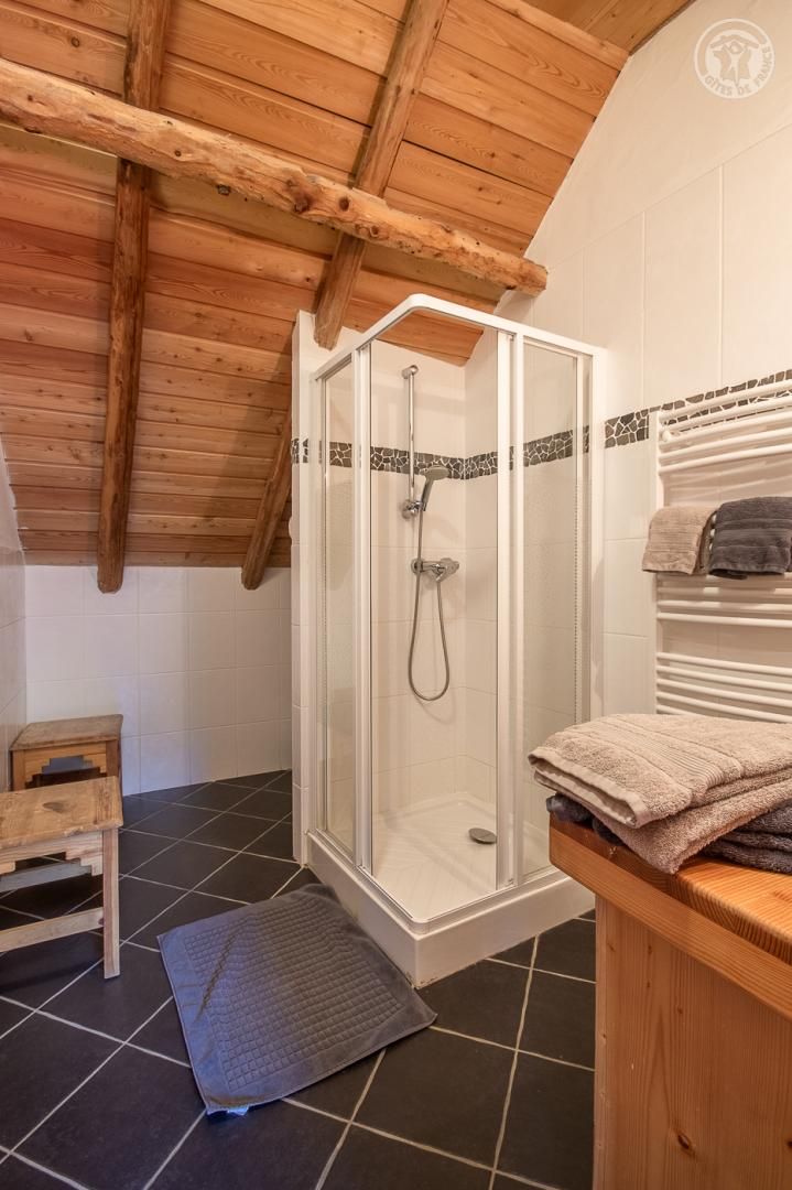 A shower with a glass enclosure, a wooden bench, and a tiled floor.