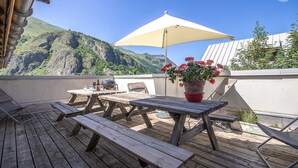 An outdoor patio with wooden tables and benches, a barbecue grill, and a potted plant with red flowers. - Chez LE Marquis DU Pontet 5 (VALLOIRE)