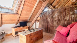 A cozy loft bedroom with a wooden ceiling, a large window, a wooden desk with a chessboard, a television, and a red sofa. - Chez LE Marquis DU Pontet 5 (VALLOIRE)
