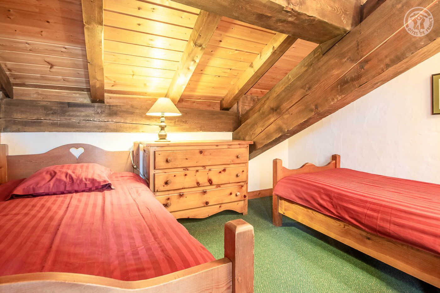 Ein gemütliches Schlafzimmer im Dachgeschoss mit zwei Holzbett, einem Schminktisch und einer Lampe.