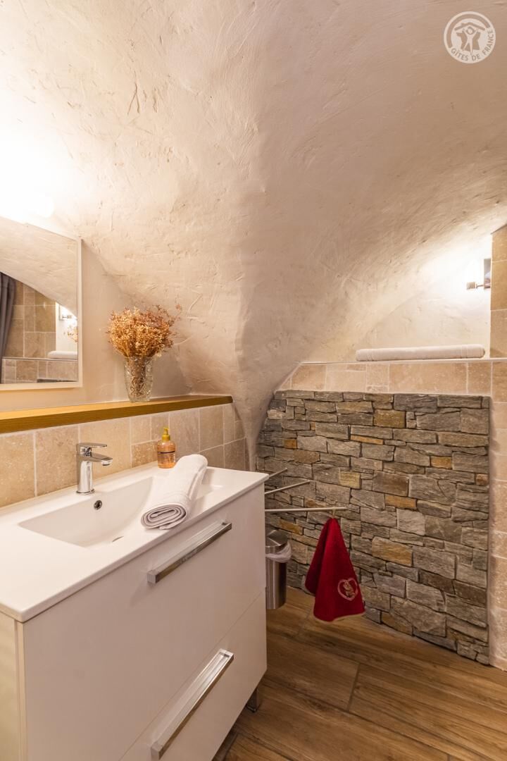 Un baño con pared de piedra, un lavabo blanco y un espejo.