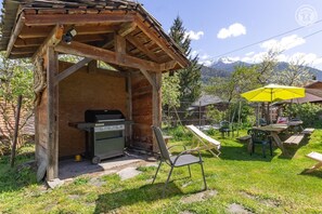 Un área de barbacoa al aire libre con parrilla, una sombrilla amarilla y una mesa de picnic con sillas.
