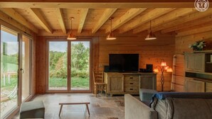 A wooden cabin interior with a stone floor, a sofa, a television, and a dining area. - LE Chalet DE LA Source (MONTAGNOLE)