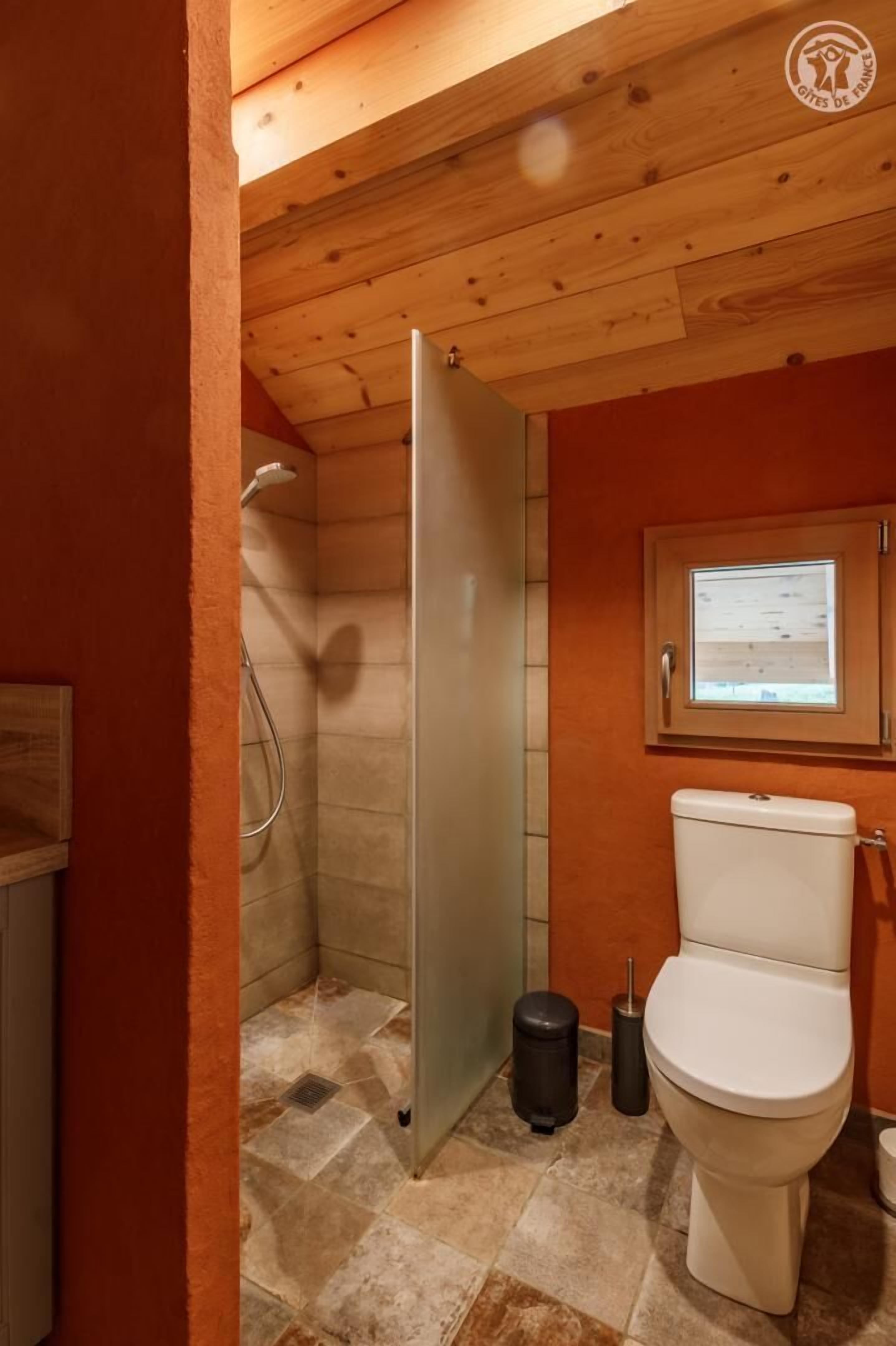 Baño pequeño con ducha, inodoro y ventana que deja entrar luz natural.