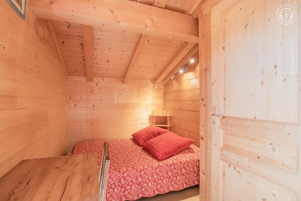 Una habitación de cabaña de madera con una cama, una mesita y un ventanal.