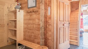 Een houten hut binnen met een houten bank, een wandplank met decoratieve decoratie, en een deur met een hartvormig bord.