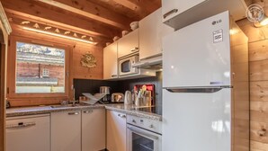 Een compacte keuken met witte apparaten, een raam met uitzicht op een gebouw en houten balken aan het plafond.