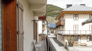 Ein Balkon mit Holztür, einer Sitzbank und Blick auf ein Gebäude mit Satteldach.