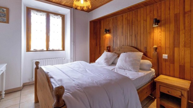 Ein Schlafzimmer mit einem Holz-Kopfteil, einem Bett mit weißer Bettwäsche, einem Nachttisch und einem Fenster mit Vorhängen.