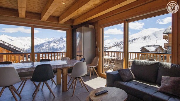 Un interior de madera con comedor, sofá y vistas a montañas nevadas.