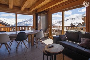 A wooden interior with a dining area, a sofa, and a view of snow-covered mountains. - LES Herens - LA Toussuire-fontcouverte (LA TOUSSUIRE FONTCOUVERTE)