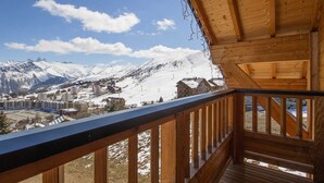 Un balcón de madera con vistas a un paisaje nevado de montañas y un pueblo en la falda.