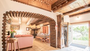 A rustic kitchen with exposed wooden beams, a stone fireplace, and a dining area with a pink sofa. - LA Grange - Traize - Gîte (TRAIZE)