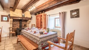 A rustic dining room with a large wooden table set for a meal, a brick fireplace, and wooden beams on the ceiling. - LA Grange - Traize - Gîte (TRAIZE)