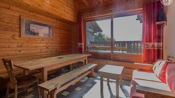 A wooden cabin with a dining area, a sofa, and a window with curtains.