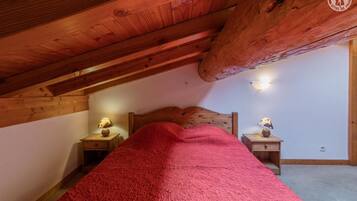 A cozy attic bedroom with a sloped ceiling, a wooden headboard, and two bedside tables with lamps.