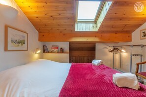 Ein Schlafzimmer mit Oberlicht, einem Bett mit weißer und rosa Bettwäsche, einem Schild mit Ski-Motiv und einem Holz-Kopfende.