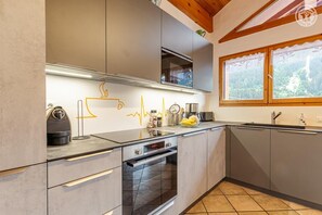 Eine moderne Küche mit Backofen, Kaffeemaschine und einem Fenster mit Blick auf den Wald.