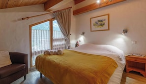 Ein Schlafzimmer mit Bett, Holz-Kopfteil, Fenster mit Vorhängen, Nachttisch und einer Wandlampe.