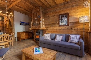 A cozy log cabin interior with a sofa, wooden dining table, and a fireplace.