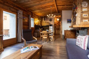A cozy cabin interior with a dining area, a sofa, and a wooden ceiling.