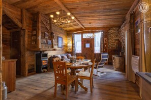 L’intérieur d’un chalet rustique en bois comprend un coin repas, des chaises en bois, un lustre et un mur en pierre.