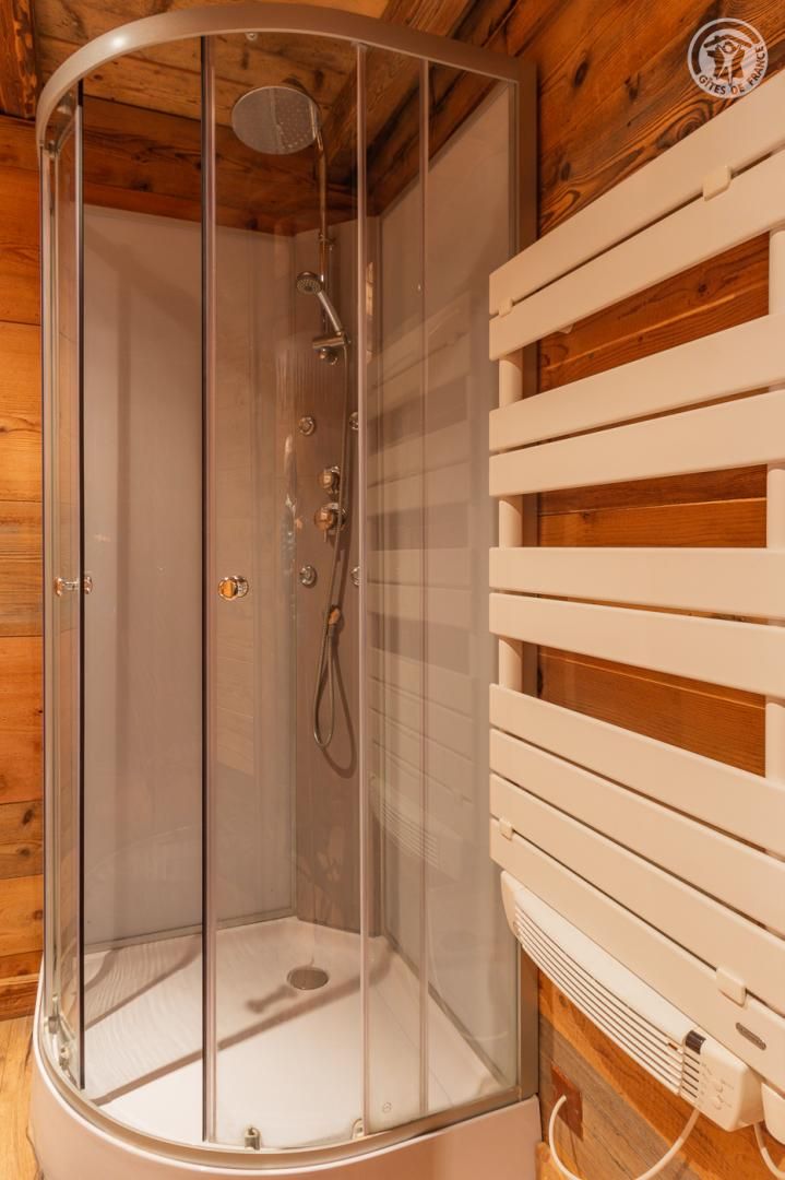 Une douche fermée par des parois de verre, avec un intérieur en bois et un mur à lattes blanches sur le côté droit.