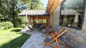 A wooden deck with lounge chairs, a stone wall, and a pergola with umbrellas.