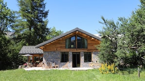 A modern log cabin with a stone foundation, large windows, and a sloped roof.