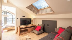 A modern living room with a skylight, a large flat-screen TV, a sofa with red cushions, and a wooden entertainment unit.