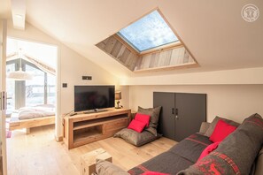 Una sala de estar moderna con tragaluz, un televisor de pantalla plana grande, un sofá con cojines rojos y un mueble de entretenimiento de madera.