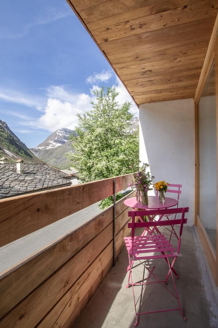 Ein Balkon mit Holzgeländer, einem Tisch mit Stühlen und einer Vase mit Blumen.