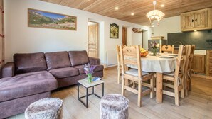 A cozy living room with a brown sofa, a small table with a vase of flowers, and a dining area with wooden chairs and a table. - LES Lauzes 1 - Bonneval SUR ARC (BONNEVAL SUR ARC)