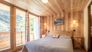 A wooden cabin bedroom with a bed, nightstands, and a painting on the wall. - LES Lauzes 1 - Bonneval SUR ARC (BONNEVAL SUR ARC)