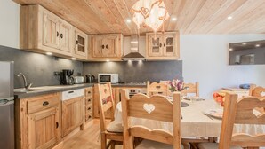 A wooden kitchen with cabinets, a dining table, chairs, and a hanging light fixture. - LES Lauzes 1 - Bonneval SUR ARC (BONNEVAL SUR ARC)