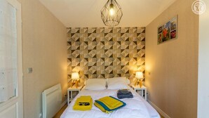 A hotel room with a geometric patterned wall, a bed with white linens, two bedside tables with lamps, and a hanging light fixture. - LE Barillon - Avrieux (AVRIEUX)