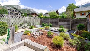 A well-maintained garden with a wooden deck, surrounded by a wooden fence, and houses in the background. - LE Barillon - Avrieux (AVRIEUX)