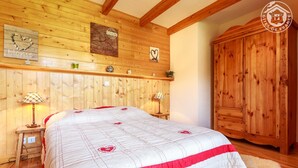 A wooden-paneled bedroom with a large bed, two bedside tables with lamps, a wooden wardrobe, and wall decorations including a heart-shaped sign and a tree-ring pattern.