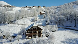 A snow-covered mountain village with traditional wooden houses, a winding path, and a clear blue sky.