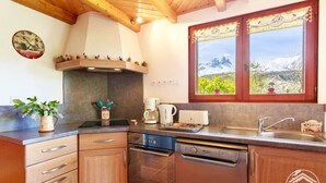 A kitchen with wooden cabinets, a stove, a coffee maker, and a window with a view of mountains.